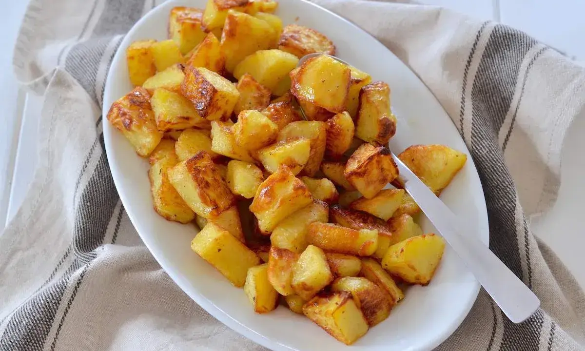 Un piatto bianco pieno di patate al forno dorate e croccanti, pronte per essere gustate.