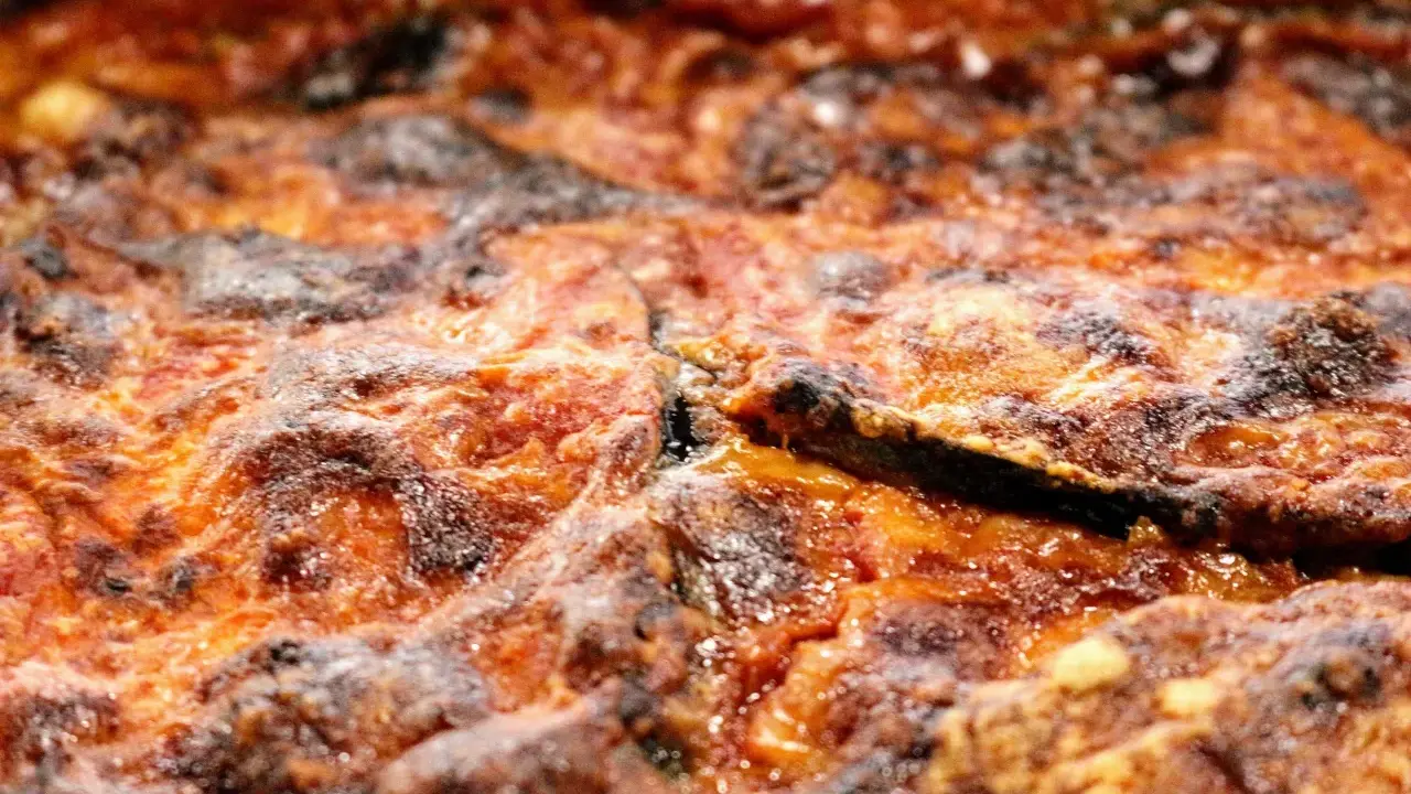 Primo piano di una parmigiana di melanzane appena sfornata, con strati dorati e croccanti.