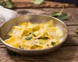 Ravioli ricotta e spinaci dorati, conditi con parmigiano e foglie di salvia fresca, serviti in una ciotola metallica su un tavolo di legno rustico.