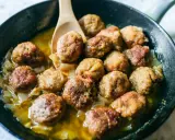 Polpette in bianco succulente in padella con cipolle caramellate, pronte per essere gustate.