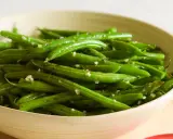 Fagiolini freschi saltati in padella con aglio e pepe, serviti in una ciotola di legno.