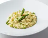 Risotto cremoso con asparagi freschi e succulenti gamberetti, guarnito con punte di asparagi croccanti.