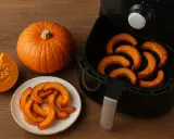 Zucca in friggitrice ad aria: fette arrostite e una intera su un tavolo di legno.