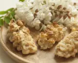 Fiori di acacia fritti, dorati e croccanti, su un piatto di legno, con grappoli di fiori freschi sullo sfondo.