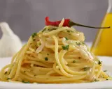 Spaghetti conditi con aglio, olio e peperoncino, guarniti con un peperoncino rosso e prezzemolo. Sullo sfondo, un bulbo d'aglio e una bottiglia d'olio.