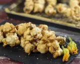 Frittelle di fiori di zucca dorate e croccanti, servite su una lavagna con fiori freschi e sale grosso.