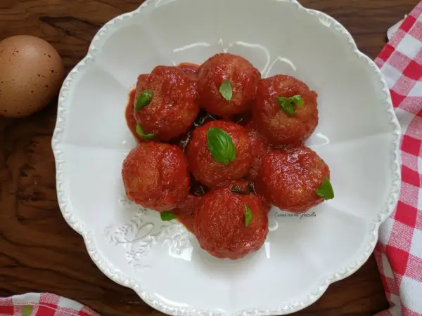Pallotte cacio e ova in salsa di pomodoro, guarnite con basilico fresco. Un uovo intero è visibile a sinistra.