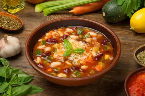 Un fumante minestrone di verdure, ricco di fagioli, zucchine e carote, guarnito con basilico fresco e parmigiano.