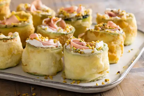 Rotolini di zucchine impanate e fritte, farciti con crema, prosciutto e pistacchi. Stuzzichini veloci ed economici perfetti per un aperitivo sfizioso.