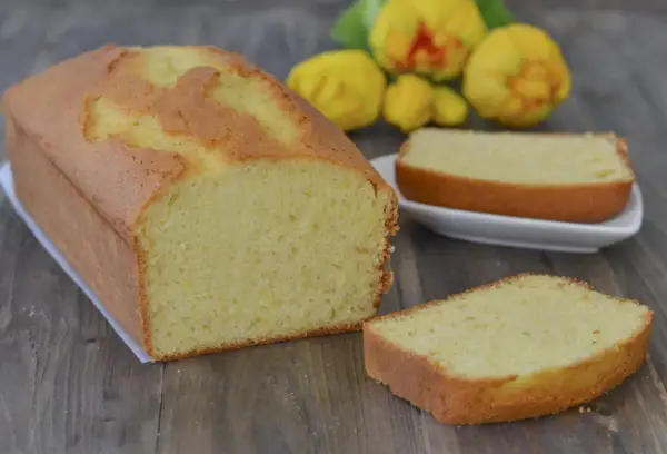 Un soffice plumcake al limone, dorato e profumato, pronto per essere gustato. Due fette sono già state tagliate, invitando a un assaggio.