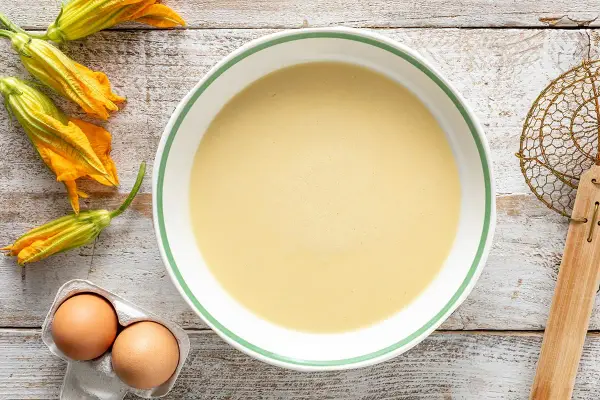 Pastella per fiori di zucca pronta in ciotola, con fiori freschi e uova a lato.