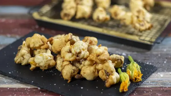 Frittelle di fiori di zucca dorate e croccanti, servite su una lavagna con fiori freschi e sale grosso.