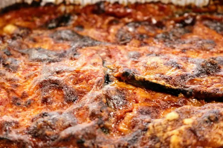 Primo piano di una parmigiana di melanzane appena sfornata, con strati dorati e croccanti.