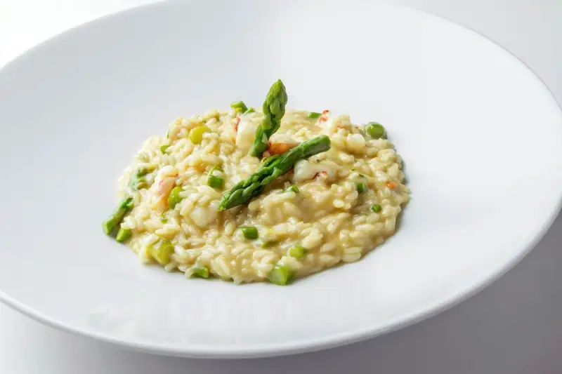 Risotto cremoso con asparagi freschi e succulenti gamberetti, guarnito con punte di asparagi croccanti.