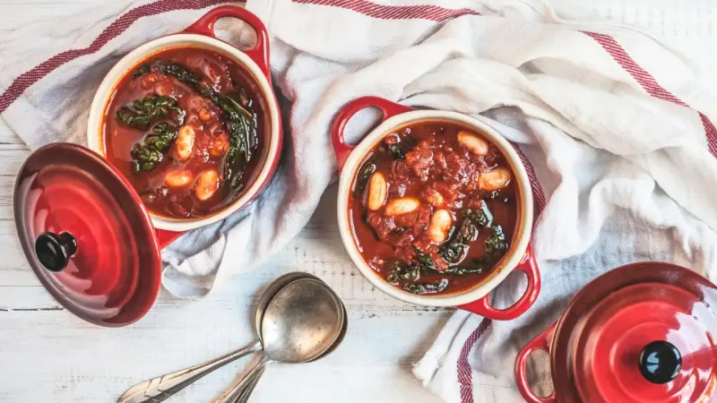 Due ciotole rosse con zuppa di cavolo nero, fagioli e pomodoro, pronte per essere gustate.
