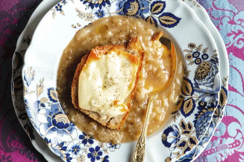 Piatto di zuppa di cipolle fumante, con crostino di pane e formaggio fuso, servita su un elegante piatto decorato.